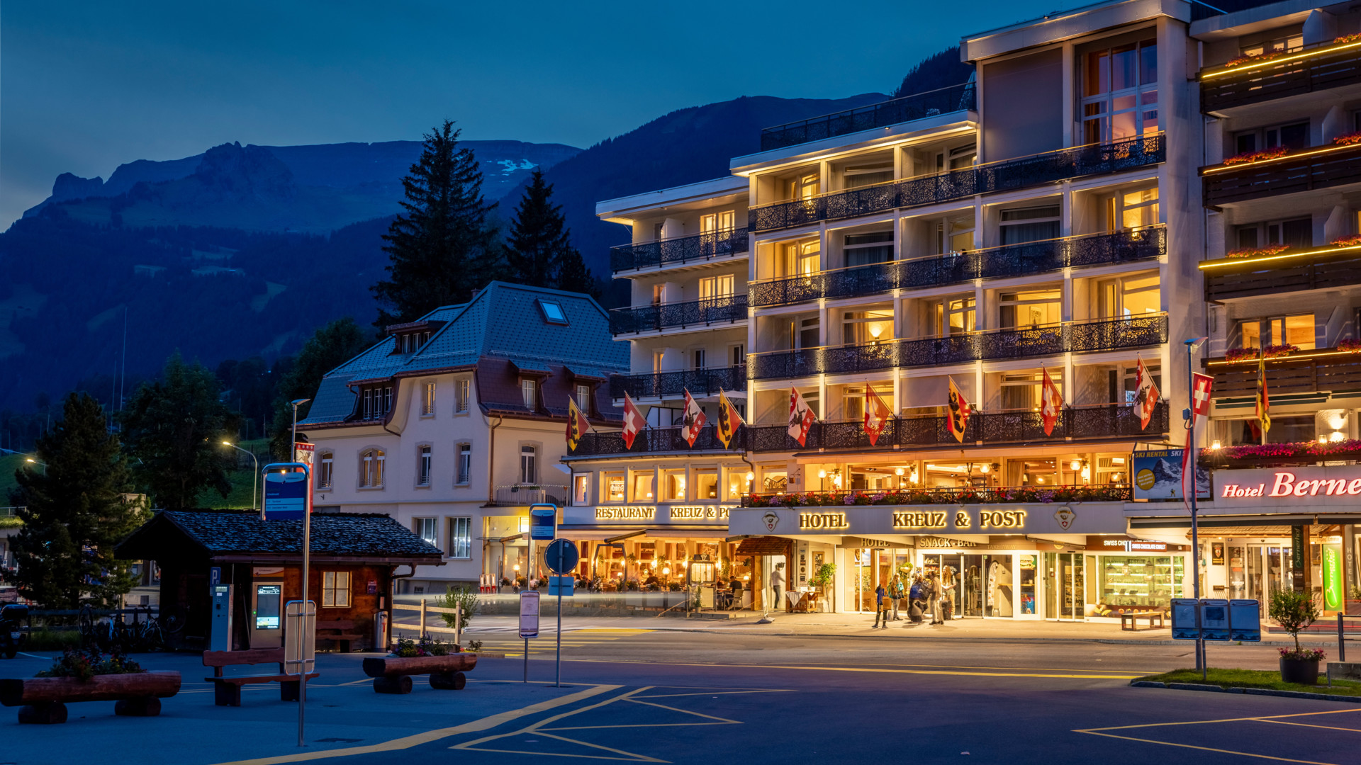 Twilight over a bustling Swiss hotel with glowing lights and mountain backdrop, evoking a warm, welcoming ambiance for travelers.