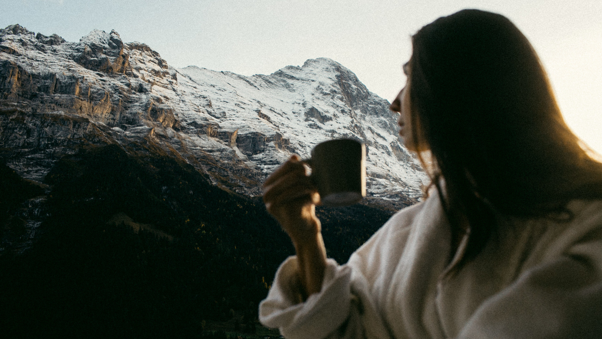 Serenity personified with a woman in white, sipping coffee against a backdrop of snow-capped mountains, radiating peace and retreat into nature.