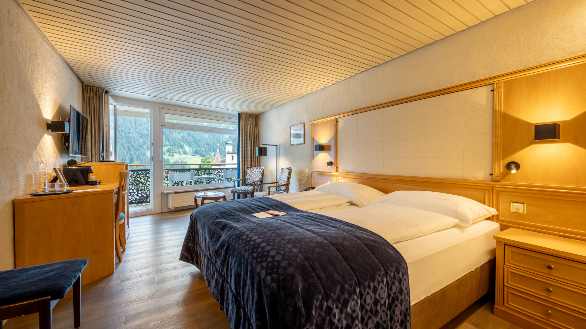 Warm-hued, cozy hotel room with elegant wooden decor and panoramic mountain views, ideal for relaxation and travel.