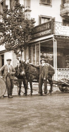 Sepia-toned historical street scene with men and horses by old-fashioned carts, evoking a nostalgic and industrious ambiance relevant to historical studies.