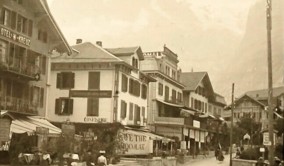Sepia-toned vintage street view of alpine town with bustling market stalls, evoking a nostalgic and tranquil atmosphere relevant to historical tourism.