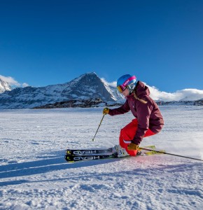Skier in bright red and purple gear glides on snow with majestic snowy mountains backdrop, exuding an energetic and adventurous vibe for winter sports enthusiasts.