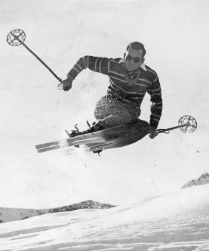 Vintage black-and-white photo of a skier in mid-jump against snowy mountain backdrop, exuding excitement and adventure, ideal for winter sports enthusiasts.