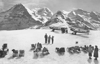 Majestic snowy mountain peaks with light aircraft and lounging visitors, evoking a serene yet adventurous atmosphere for travel and leisure.