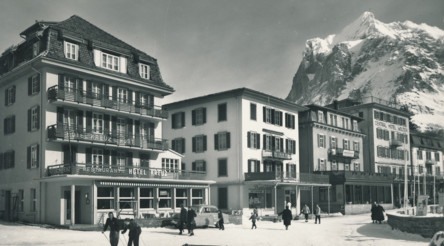 Vintage town square framed by snowy mountains, with quaint hotels in muted colors creating a serene, nostalgic vibe for travel history enthusiasts.