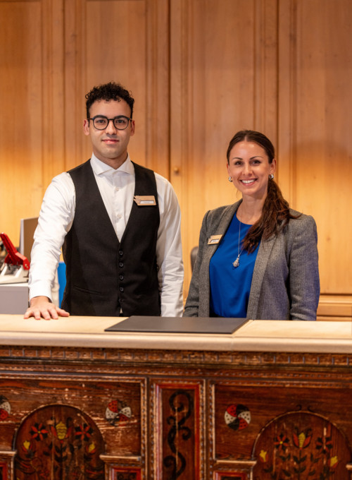 Professional hotel staff at a carved wooden reception desk, exuding a welcoming and efficient service atmosphere for the hospitality industry.