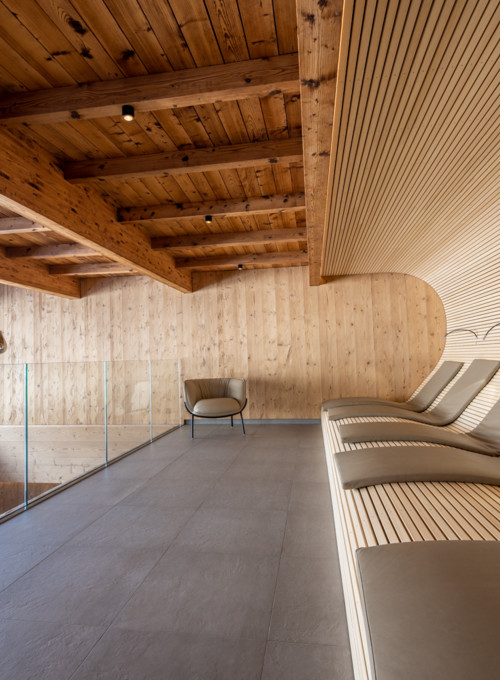 Curved wooden lounge area with sleek glass barriers, exuding warmth and modern tranquility for luxury hospitality settings.