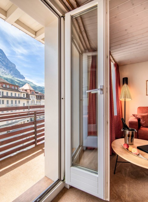 Cozy mountain-view room with vibrant red sofa and wooden accents, evoking warmth and tranquility in a vacation setting.