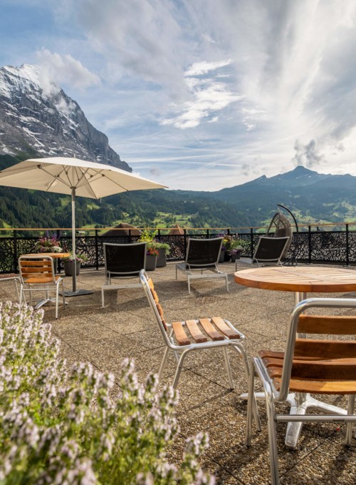 Mountain-view terrace with umbrella-shaded seating, evoking relaxation and alpine charm for travel and leisure.
