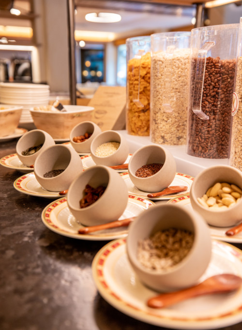 Warm, inviting breakfast buffet with ceramic bowls of seeds and nuts, set against a backdrop of cereal dispensers; ideal for health-conscious diners.