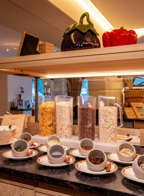 Warmly lit buffet setup with cereals in clear dispensers and assorted toppings, inviting a wholesome breakfast experience for hotel guests.