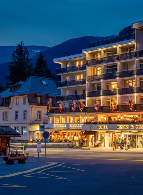 Twilight scene at a bustling hotel with warm lighting, set against a backdrop of serene mountains, capturing a welcoming atmosphere for travelers.