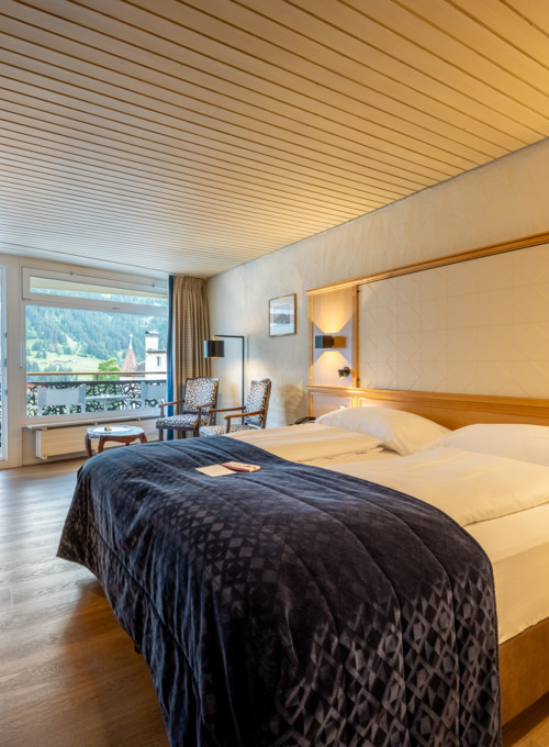 Cozy hotel room with warm wood tones and plush blue bedding, offering a serene view, ideal for leisure travelers.