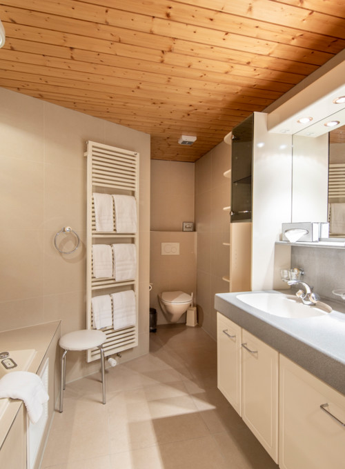 Warm, cozy bathroom with wooden ceiling and beige tiles, offering a serene, spa-like atmosphere for relaxation.
