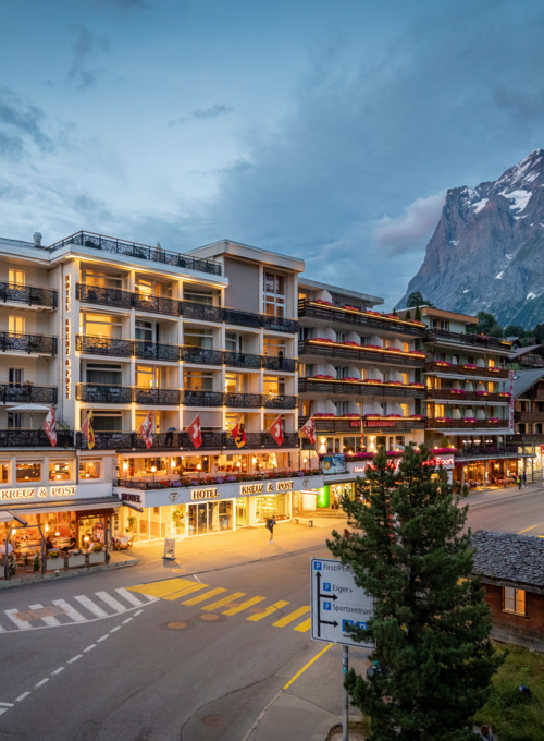 Twilight over a bustling hotel with lit balconies, nestled against a dramatic mountain backdrop, evokes a sense of adventurous escape in a tourist haven.
