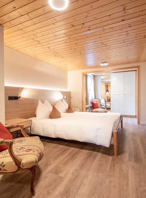 Cozy hotel room with wooden ceilings, warm lighting, and a vintage armchair, creating a welcoming ambiance for travelers.