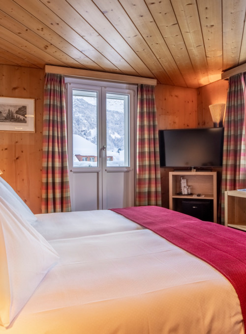 Cozy alpine hotel room with warm wooden interiors and red accents, offering a serene and inviting mountain getaway.