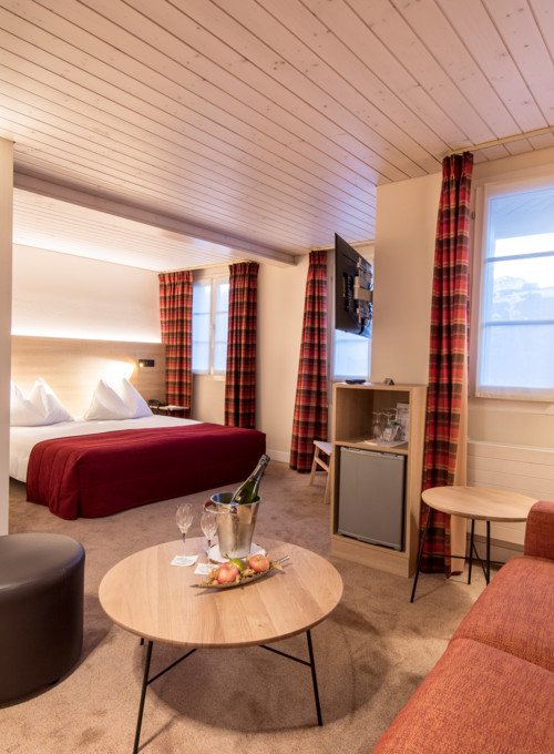 Cozy hotel room with a rich red bed, tartan curtains, and soft lighting, offering a warm, inviting atmosphere for travelers.