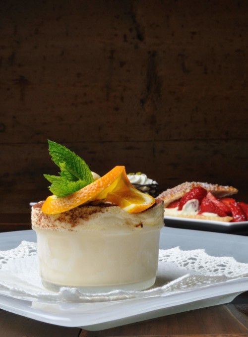 Elegant dessert display with a creamy tiramisu topped with an orange slice and mint, against a rustic backdrop, perfect for culinary presentations.