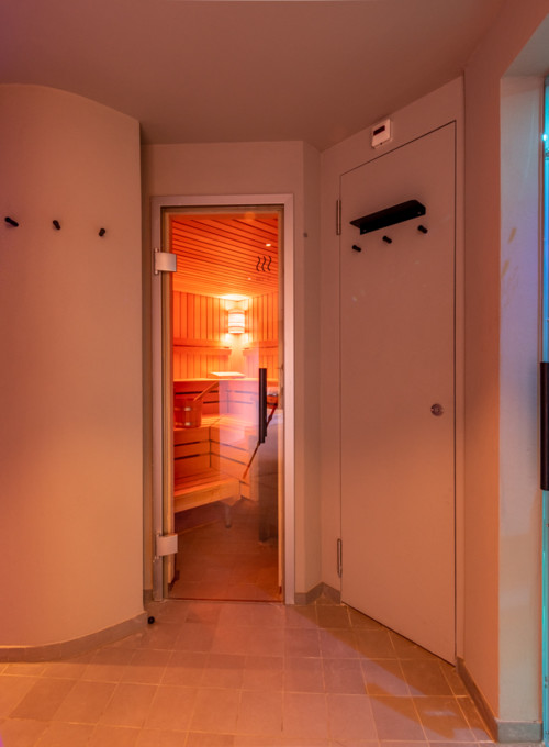 Mood-lit spa corridor featuring warm wooden sauna and cool blue-lit pool, inviting relaxation in a luxury wellness center.