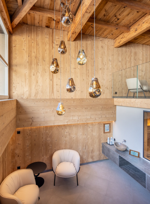 Warm wooden interiors with suspended golden lights, this serene spa-like setting offers relaxation against a snowy mountain backdrop.