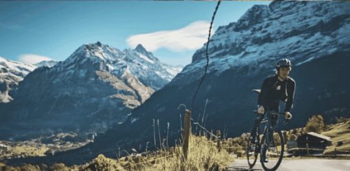 Cyclist traversing a serene mountain road with snow-capped peaks, embodying freedom and adventure ideal for outdoor sports enthusiasts.