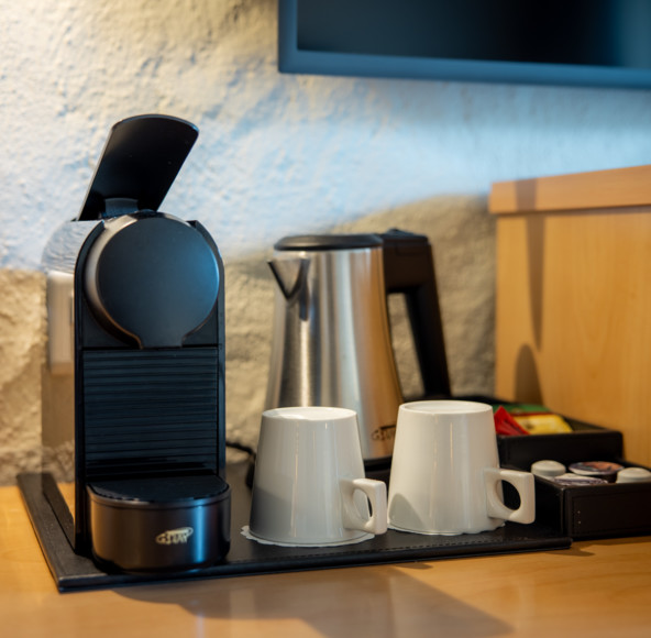Compact office coffee station with black espresso machine and white mugs, set against a textured blue wall, offering a cozy, inviting break space.