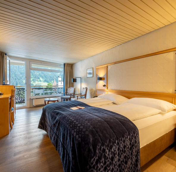 Warm-hued, cozy hotel room with elegant wooden decor and panoramic mountain views, ideal for relaxation and travel.