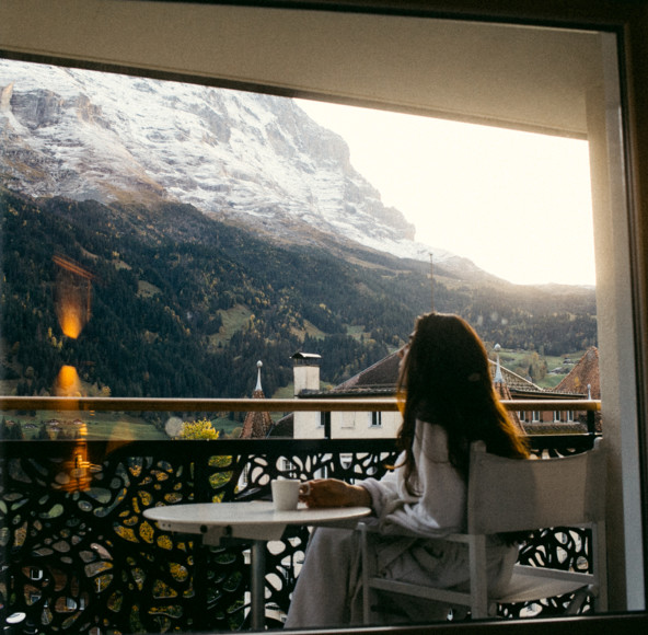Woman enjoys a serene morning view of snowy mountains from a balcony, evoking peace and relaxation, ideal for travel and leisure sectors.