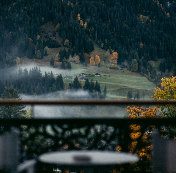 Misty autumn landscape viewed from a balcony, featuring vibrant fall trees against a serene mountain backdrop, ideal for travel and nature themes.