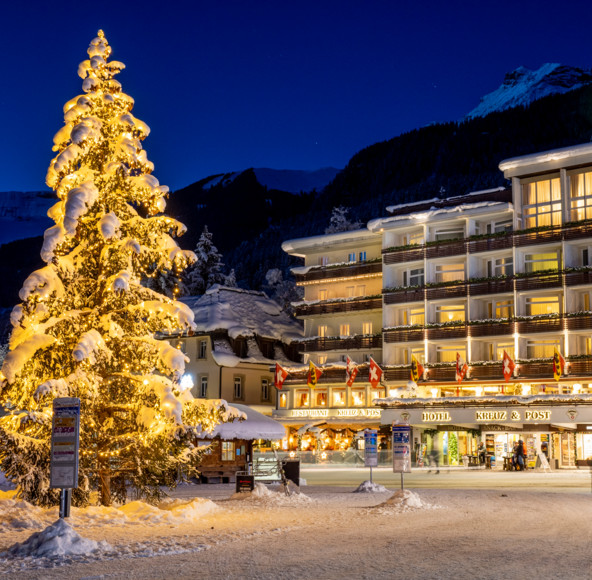Snow-covered Christmas tree illuminated by golden lights against a backdrop of quaint, festive hotels, evoking a cozy, welcoming winter ambiance ideal for holiday tourism.