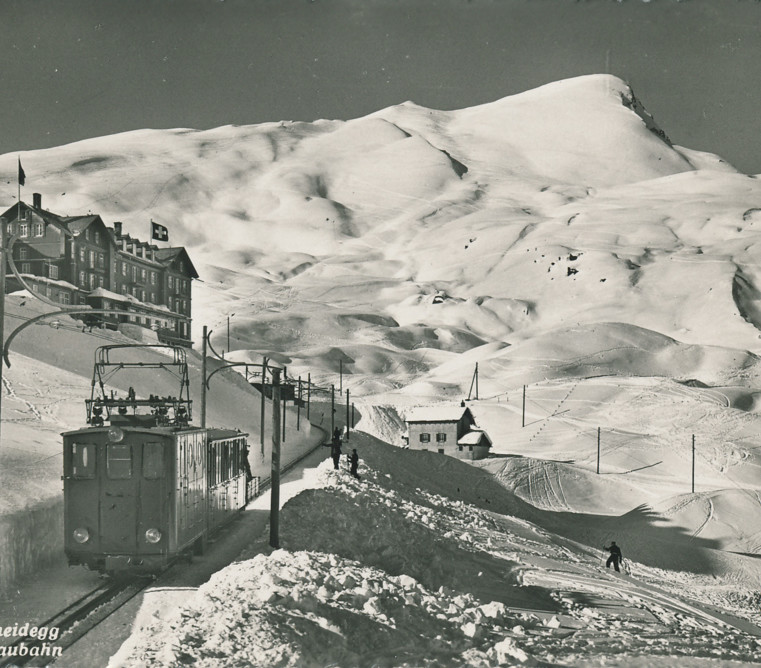 Vintage black-and-white photo of a snow-covered alpine landscape with a tram, exuding a serene, historical charm, ideal for travel and history enthusiasts.
