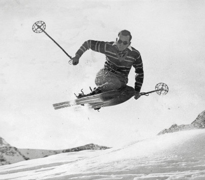 Vintage black-and-white photo of a skier in mid-jump against snowy mountain backdrop, exuding excitement and adventure, ideal for winter sports enthusiasts.