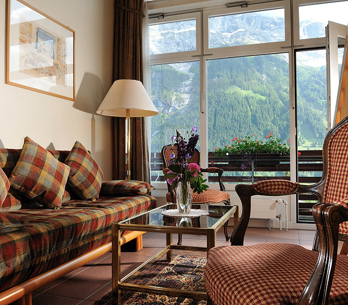 Cozy mountain-view living room with plaid couches and glass window facade, evoking a serene, inviting atmosphere for relaxation and tourism.