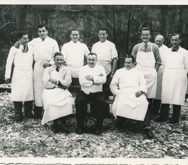 Vintage black-and-white photo of smiling chefs in white aprons, exuding camaraderie and time-honored culinary tradition.