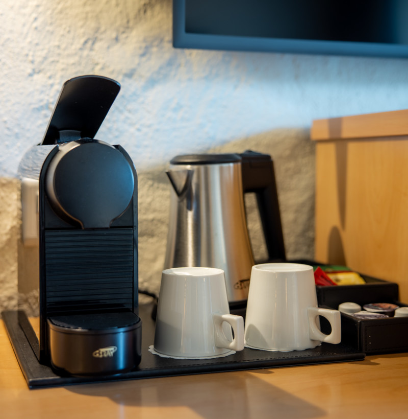 Compact office coffee station with black espresso machine and white mugs, set against a textured blue wall, offering a cozy, inviting break space.