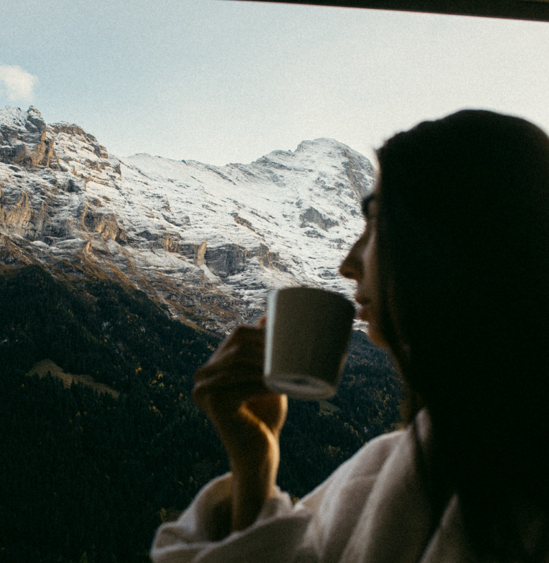 Woman drinking from a mug, silhouetted against a snow-capped mountain, capturing tranquility and the essence of leisure travel.