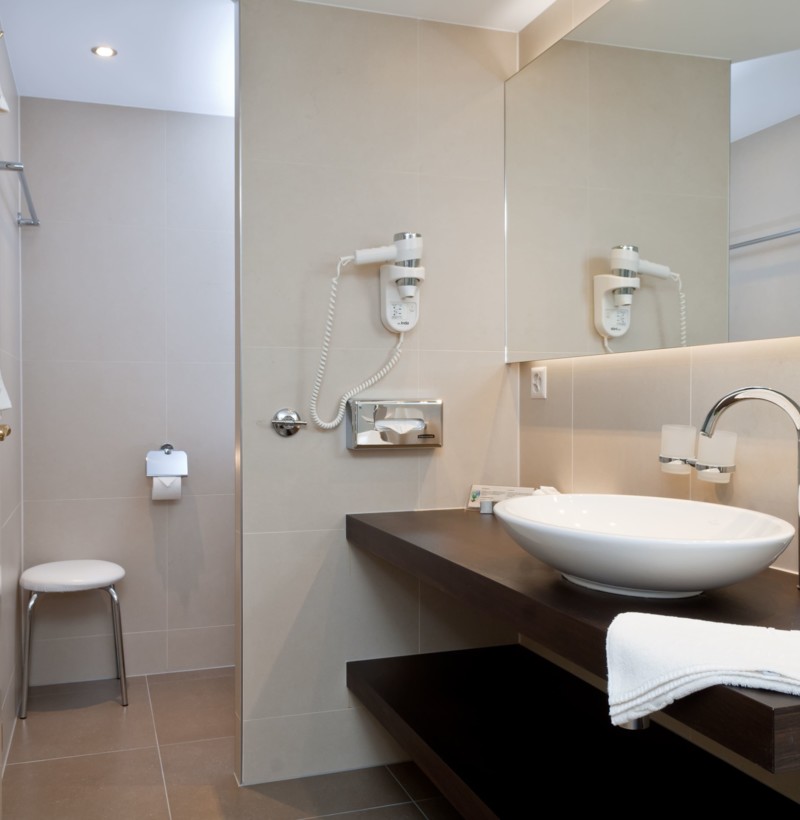 Neutral-toned bathroom with sleek fixtures and ample light, exuding a serene and modern appeal for the hospitality industry.