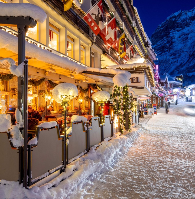 Winter evening in a cozy, snow-lined street with warmly lit cafés and shops, inviting a festive mood for holiday shopping.