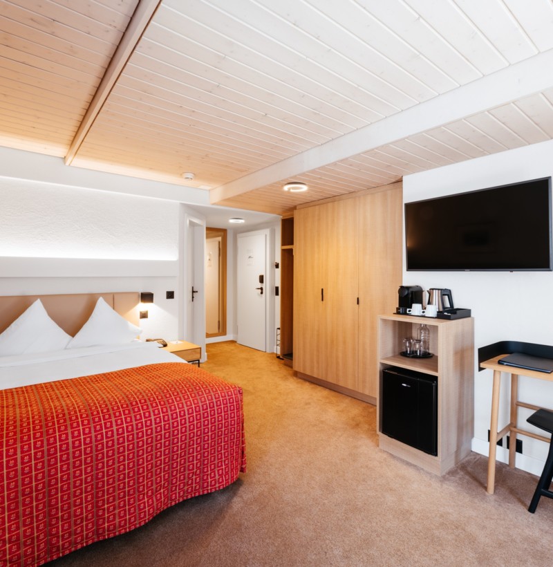 Cozy hotel room with warm wooden accents and a vibrant red bedspread, offering a welcoming and modern atmosphere for travelers.