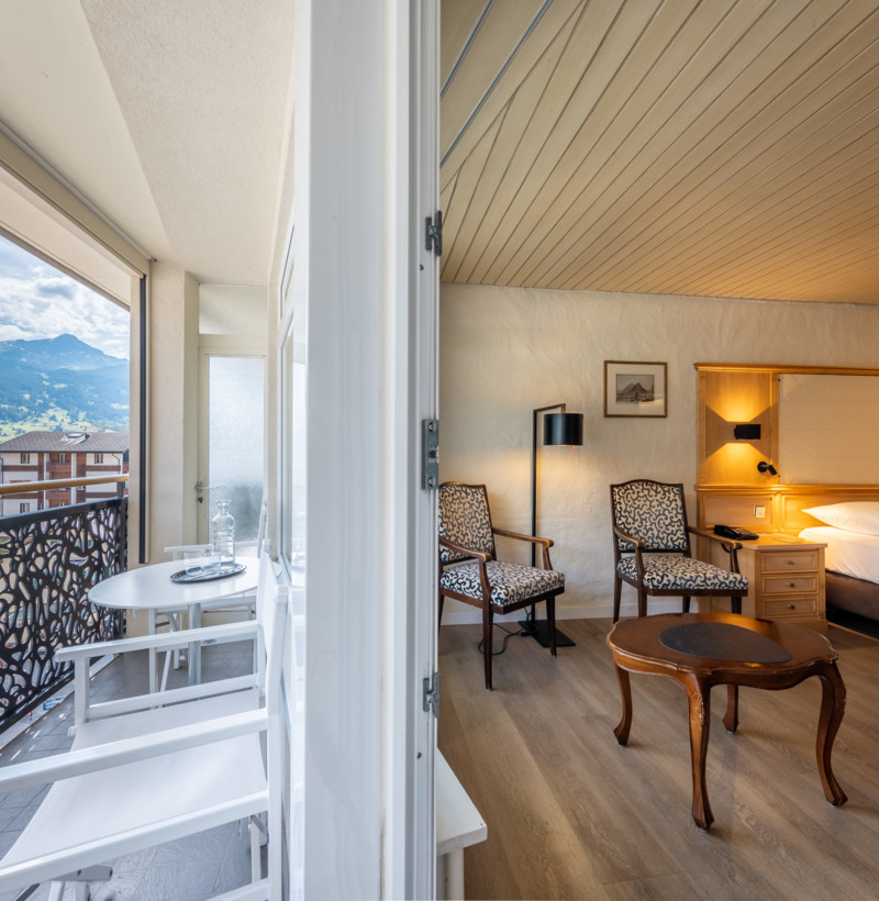 Cozy hotel room with open balcony overlooking scenic mountains, styled with warm lighting and classic furniture—perfect for relaxation and travel.