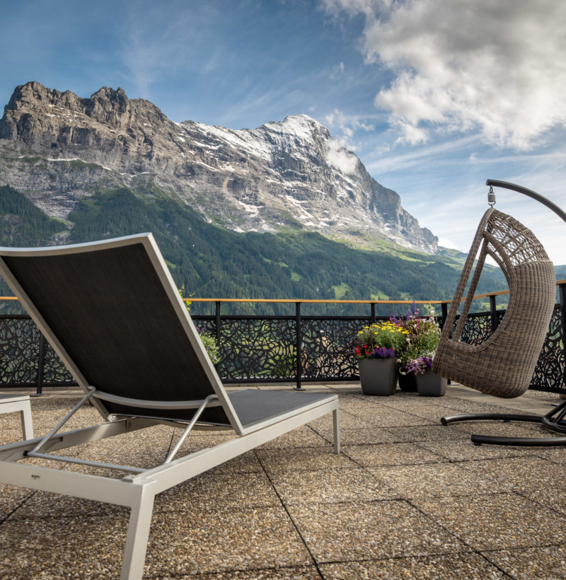 Tranquil terrace with sleek outdoor furniture overlooking majestic mountains, ideal for relaxation and tourism promotion.