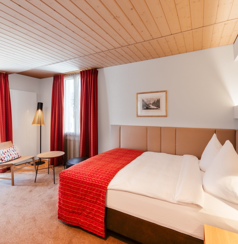 Cozy hotel room with a red bedspread and wooden accents, exuding warmth and comfort for travelers.