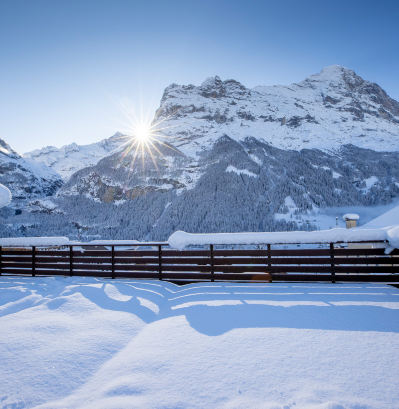 Winter wonderland with a sunburst over snow-draped mountains, radiating serenity for travel and leisure contexts.