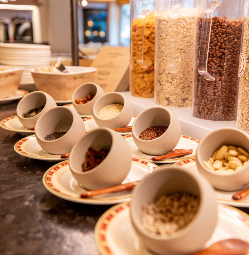 Warm, inviting breakfast buffet with ceramic bowls of seeds and nuts, set against a backdrop of cereal dispensers; ideal for health-conscious diners.