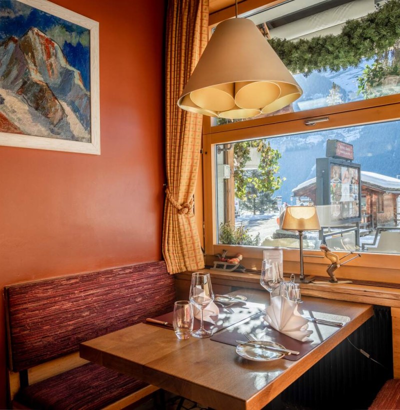 Cozy alpine restaurant corner with warm lighting and mountain views, ideal for ski enthusiasts seeking relaxation.
