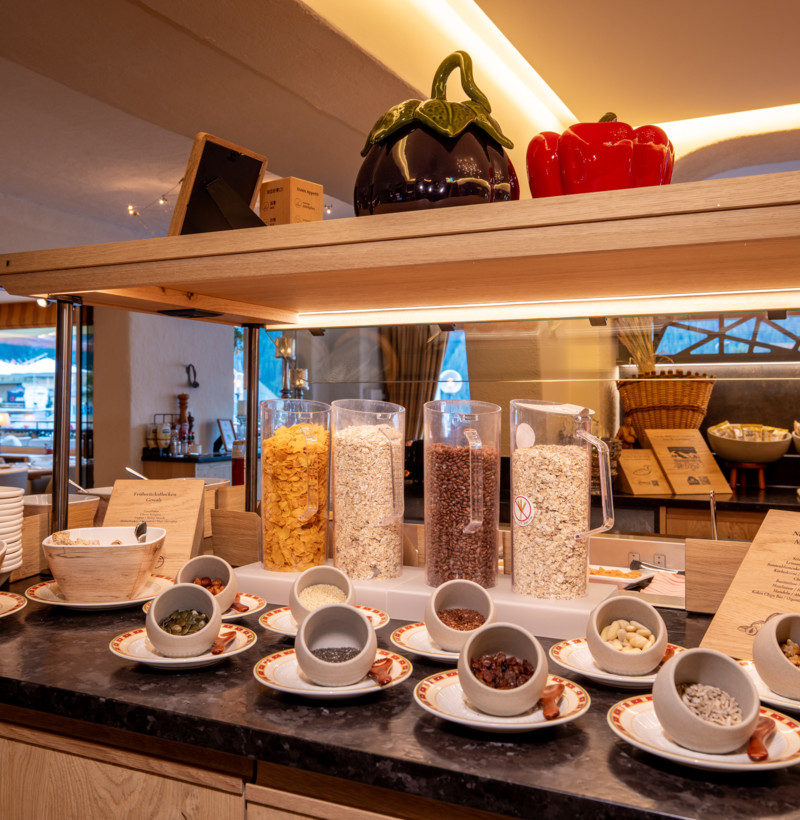 Warmly lit buffet setup with cereals in clear dispensers and assorted toppings, inviting a wholesome breakfast experience for hotel guests.