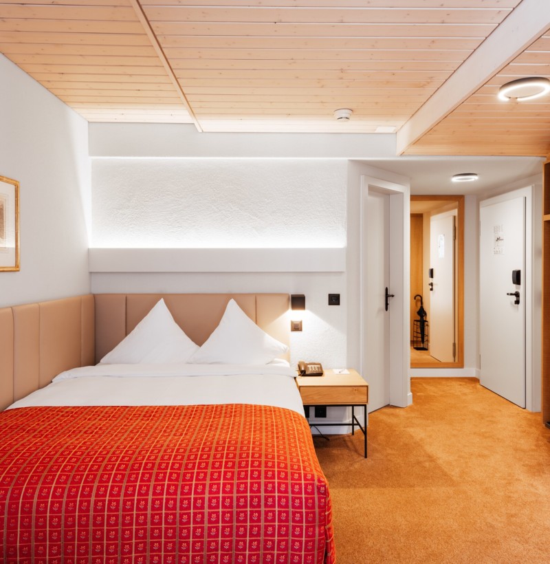 Cozy hotel room with a vibrant red bedspread and warm wooden accents, promoting relaxation for travelers.