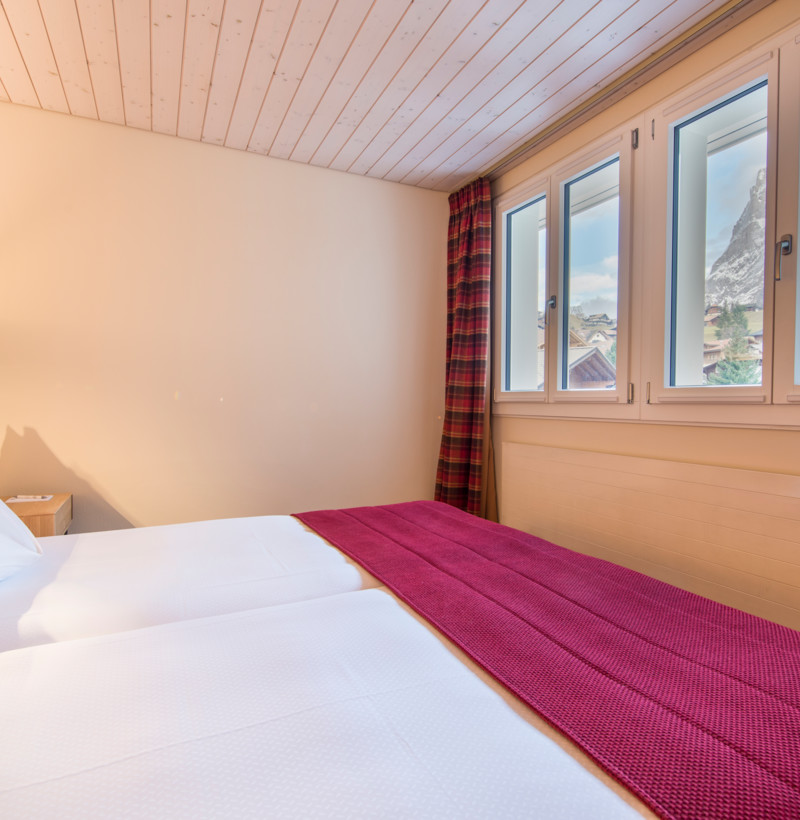 Cozy bedroom with crisp white bedding and tartan curtains, offering a tranquil mountain view, ideal for a restful retreat.