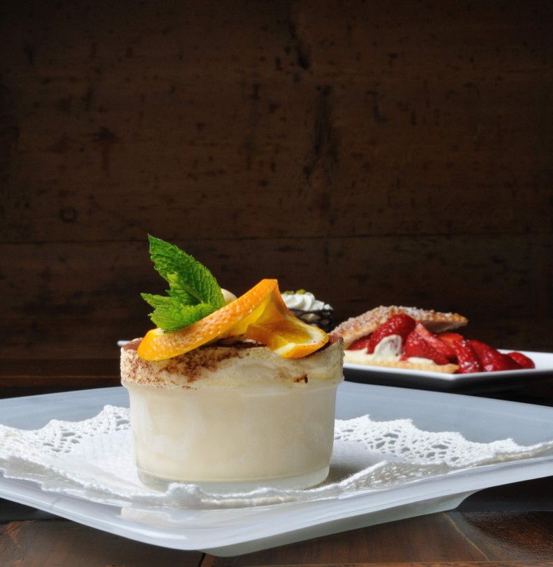 Elegant dessert presentation with a fresh, orange-garnished tiramisu in the foreground, creating an inviting ambiance for culinary aficionados.